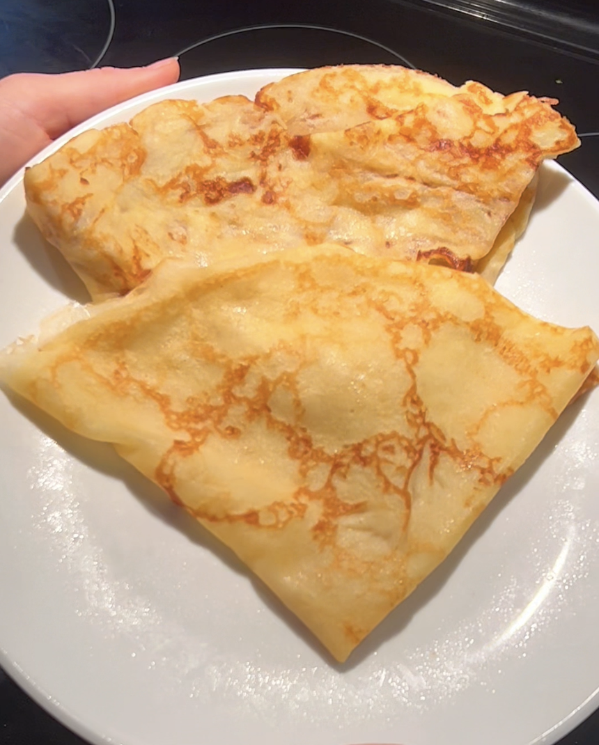 Two golden sourdough discard crepes folded and stacked on a white plate, ready for sweet or savory fillings.